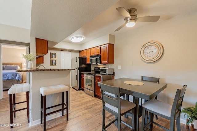 kitchen featuring brown cabinets, a peninsula, stainless steel appliances, a kitchen breakfast bar, and light wood-type flooring