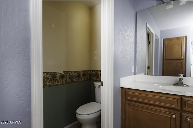 bathroom with a textured wall, vanity, and toilet