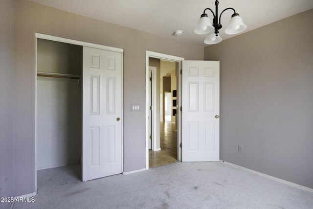 unfurnished bedroom with a chandelier, a closet, baseboards, and carpet floors