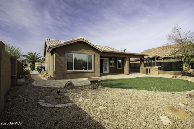 rear view of property featuring stucco siding, a patio area, a fenced backyard, and a tile roof