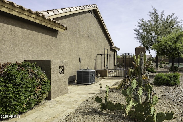 view of side of home featuring central AC unit, a tile roof, fence, stucco siding, and a gate
