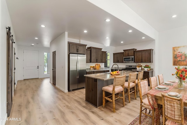 kitchen featuring a barn door, appliances with stainless steel finishes, light hardwood / wood-style floors, a kitchen bar, and a center island with sink