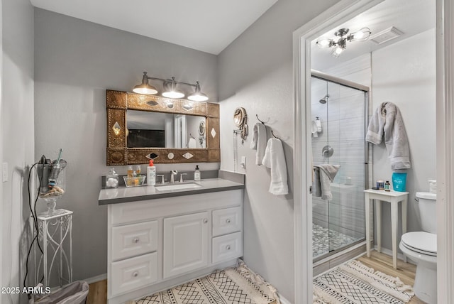 full bathroom featuring visible vents, toilet, wood finished floors, vanity, and a shower stall