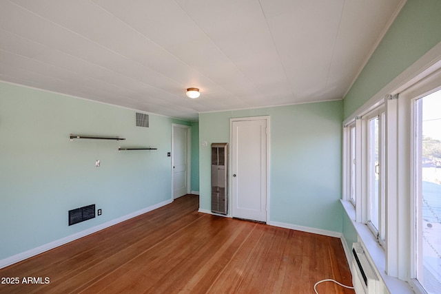 unfurnished room featuring hardwood / wood-style floors and a baseboard heating unit