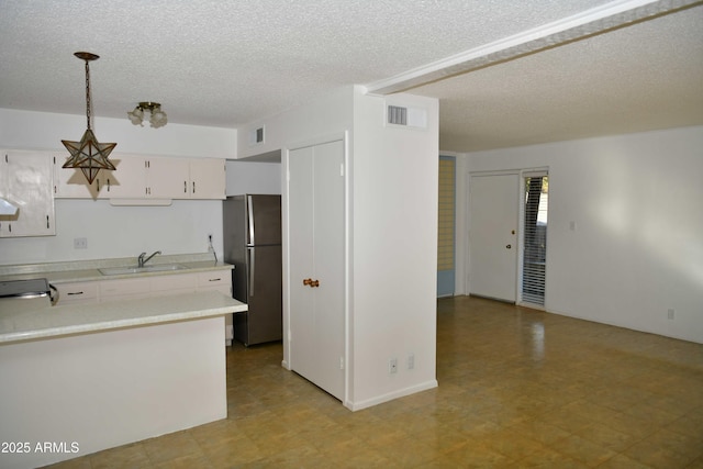 kitchen featuring sink, hanging light fixtures, a textured ceiling, white cabinetry, and stainless steel refrigerator