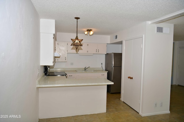 kitchen featuring sink, hanging light fixtures, kitchen peninsula, stainless steel fridge, and white cabinets