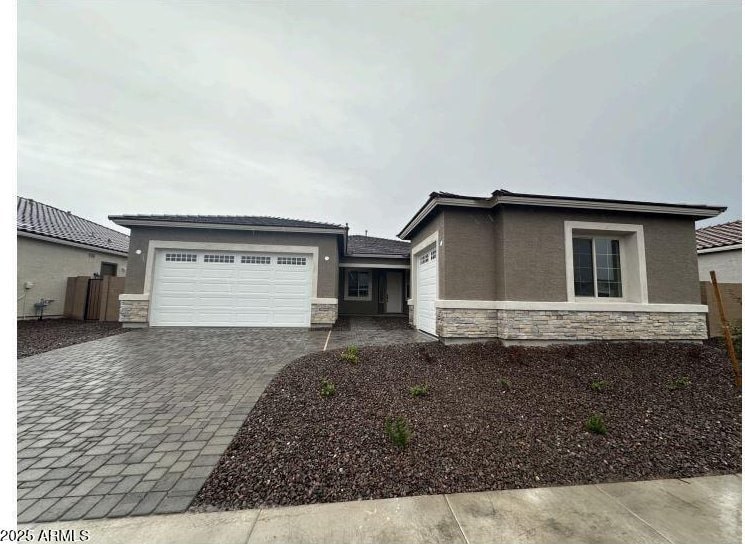 view of front of house with fence, stucco siding, decorative driveway, a garage, and stone siding