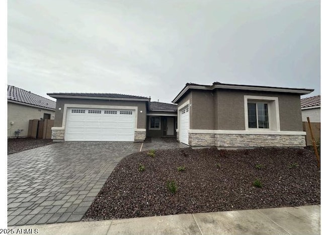 prairie-style house with an attached garage, stucco siding, decorative driveway, and stone siding