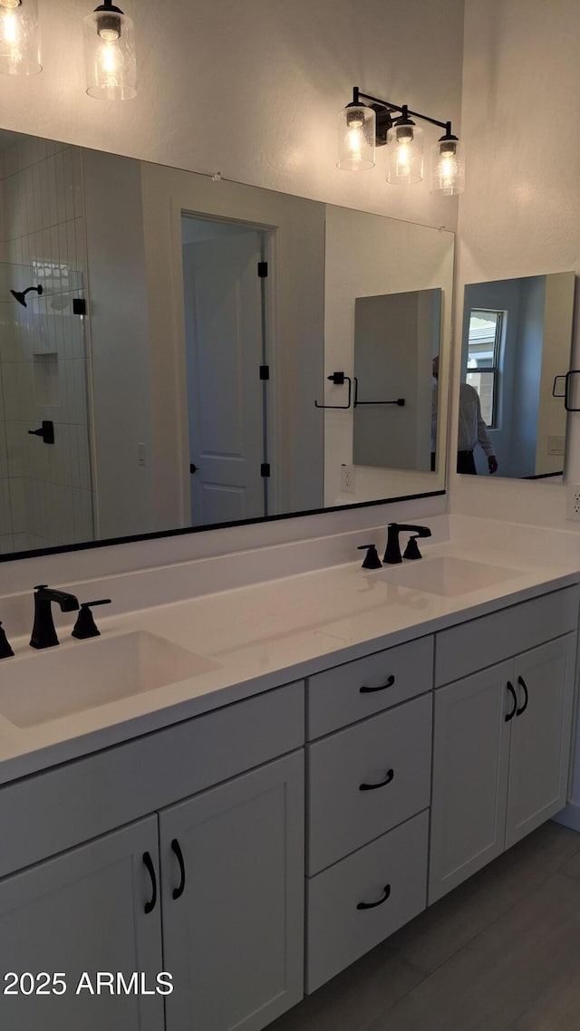 full bath with a tile shower, double vanity, and a sink