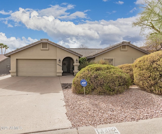 view of front of property with driveway, an attached garage, a tiled roof, and stucco siding