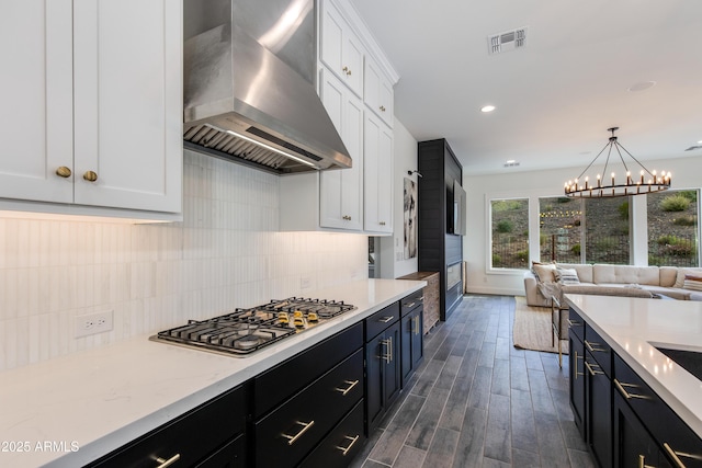 3281 Maverick Dr, Wickenburg, AZ 85390 - kitchen featuring tasteful backsplash, stainless steel gas cooktop, visible vents, wall chimney range hood, and white cabinets