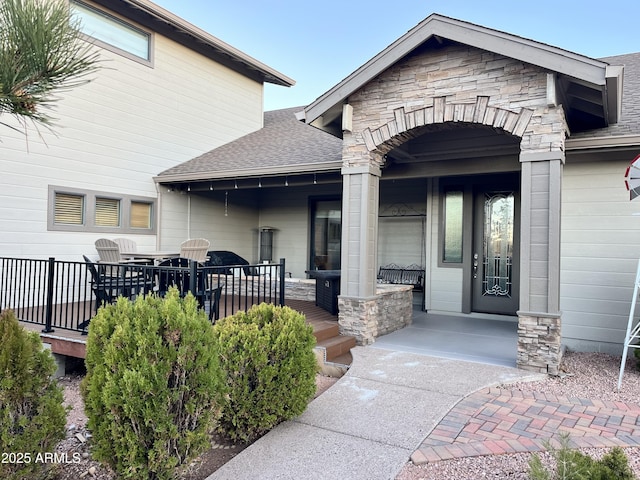 property entrance with covered porch, stone siding, and roof with shingles