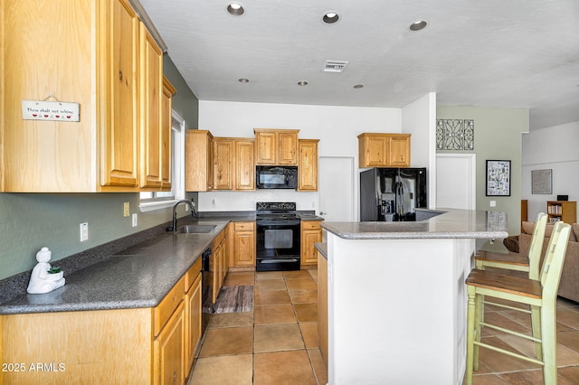 kitchen with visible vents, a kitchen island, a sink, black appliances, and a kitchen breakfast bar