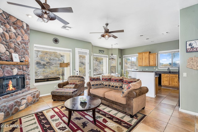 living area featuring light tile patterned floors, ceiling fan, visible vents, and a stone fireplace