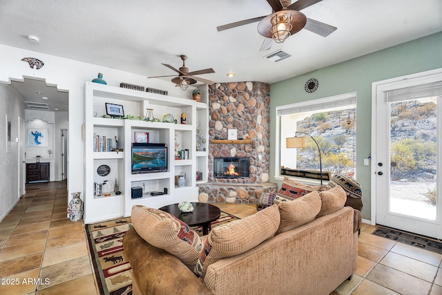 living area with ceiling fan, a fireplace, visible vents, and a healthy amount of sunlight