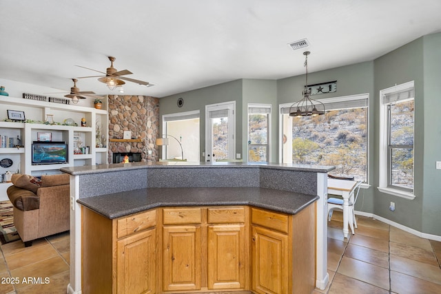 kitchen featuring a healthy amount of sunlight, visible vents, ceiling fan, and a stone fireplace