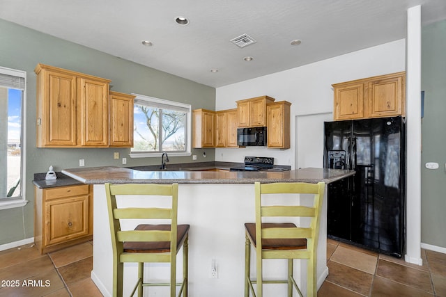 kitchen featuring black appliances, a kitchen island, visible vents, and a breakfast bar