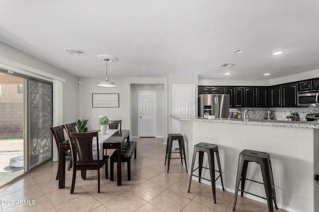 kitchen with stainless steel appliances, backsplash, light tile patterned flooring, dark cabinetry, and a kitchen bar