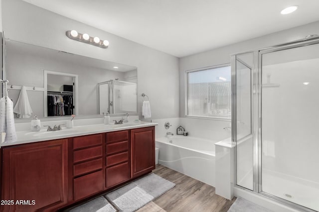 bathroom with double vanity, a stall shower, a sink, wood finished floors, and a bath