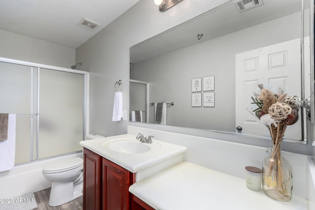 bathroom featuring toilet, enclosed tub / shower combo, visible vents, and vanity