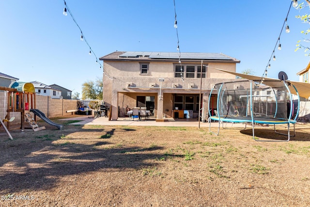 rear view of property with stucco siding, a trampoline, a playground, and a patio