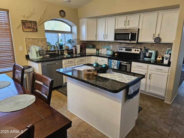 kitchen featuring lofted ceiling, white cabinetry, a center island, stainless steel appliances, and decorative backsplash