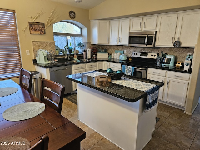 kitchen with appliances with stainless steel finishes, a center island, white cabinets, decorative backsplash, and vaulted ceiling