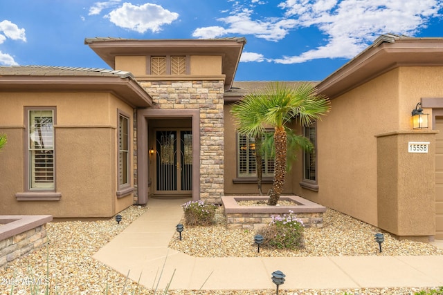 property entrance with a garage, stone siding, and stucco siding