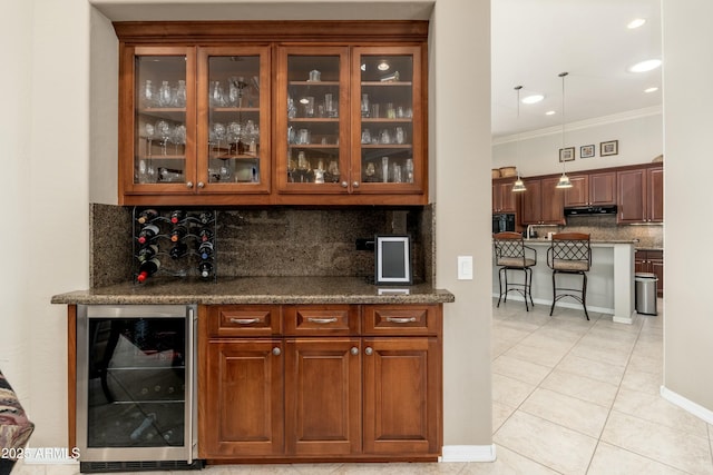 bar featuring light tile patterned floors, under cabinet range hood, beverage cooler, hanging light fixtures, and crown molding