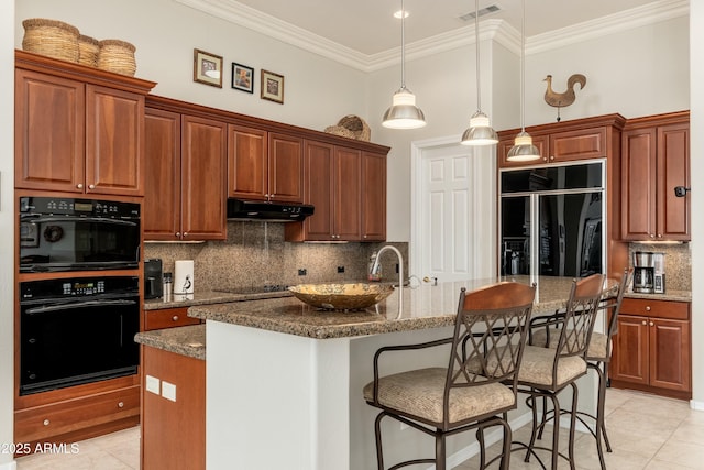 kitchen featuring black appliances, a center island with sink, dark stone counters, hanging light fixtures, and under cabinet range hood