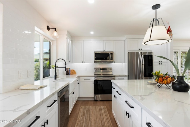 kitchen with appliances with stainless steel finishes, white cabinetry, pendant lighting, and light stone counters