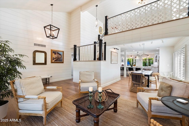 living room with wooden walls, high vaulted ceiling, a notable chandelier, and hardwood / wood-style flooring