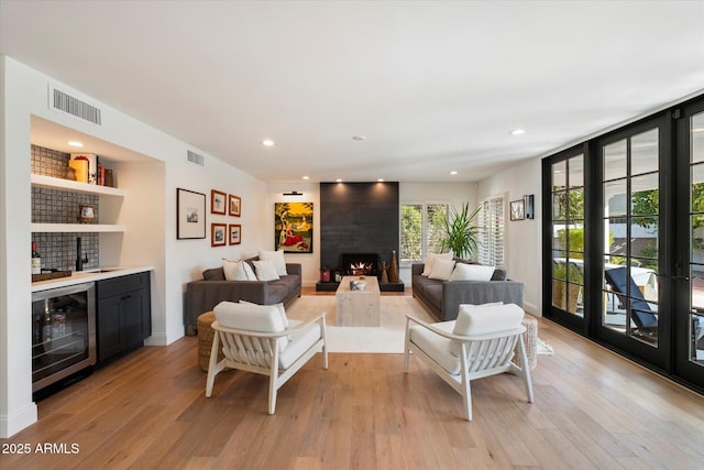 living room featuring a large fireplace, light hardwood / wood-style flooring, wine cooler, and bar area