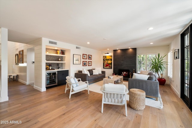 living room featuring wine cooler, a fireplace, indoor bar, and light wood-type flooring