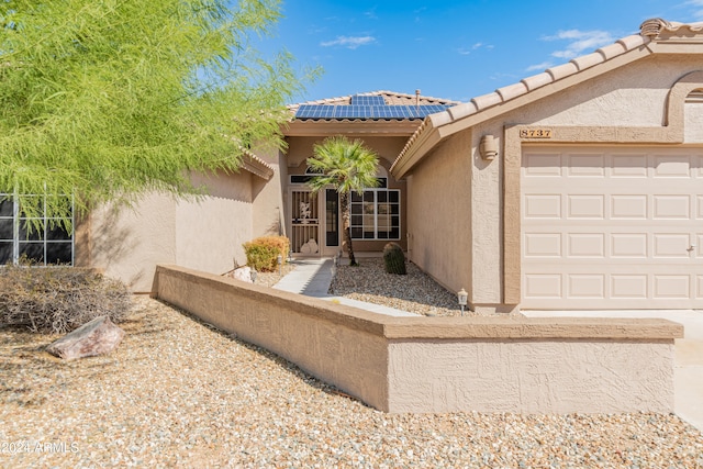 view of exterior entry featuring solar panels and a garage