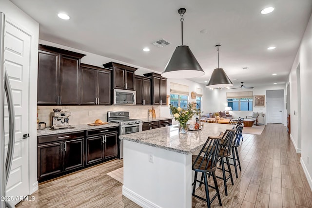 kitchen with a breakfast bar, stainless steel appliances, visible vents, hanging light fixtures, and open floor plan