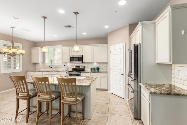 kitchen featuring a breakfast bar, backsplash, appliances with stainless steel finishes, a kitchen island with sink, and light stone countertops