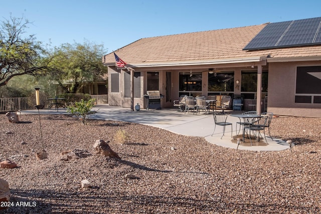 back of property featuring ceiling fan, fence, a patio area, roof mounted solar panels, and stucco siding