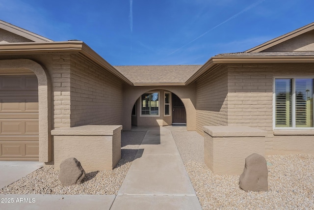 property entrance featuring a shingled roof, brick siding, and an attached garage