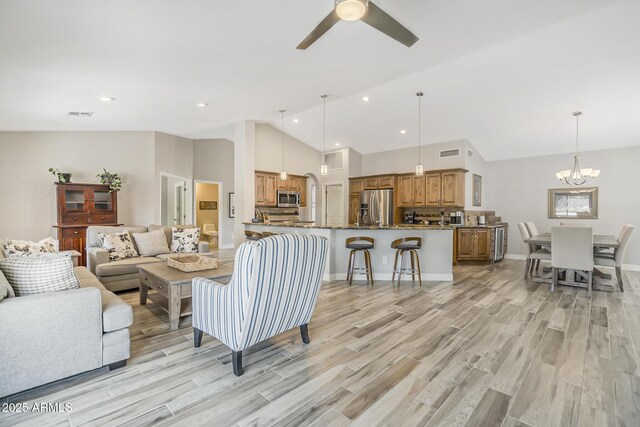 living room featuring vaulted ceiling, a chandelier, a ceiling fan, light wood finished floors, and baseboards