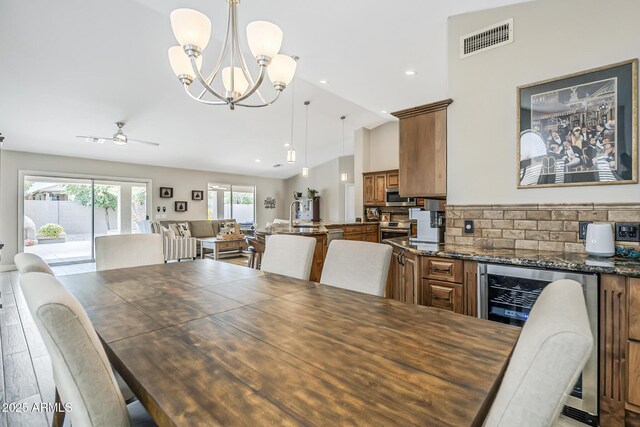 dining space featuring wine cooler, lofted ceiling, a chandelier, recessed lighting, and wood finished floors