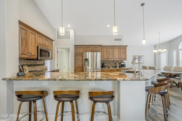 kitchen featuring appliances with stainless steel finishes, a sink, decorative backsplash, stone countertops, and lofted ceiling