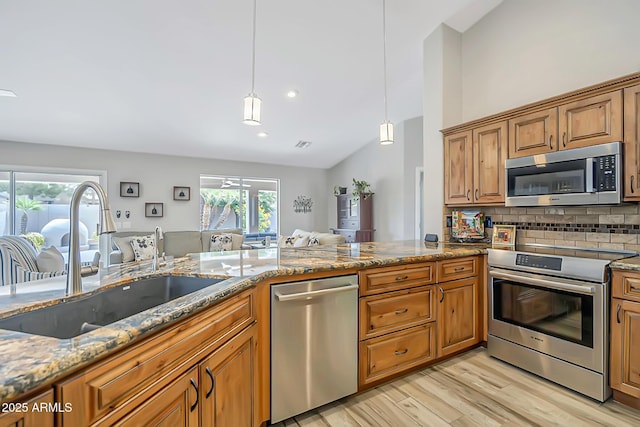 kitchen with appliances with stainless steel finishes, a sink, brown cabinets, light wood finished floors, and light stone counters