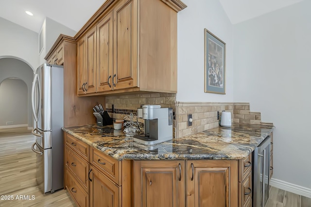 kitchen featuring freestanding refrigerator, stone countertops, brown cabinets, tasteful backsplash, and recessed lighting
