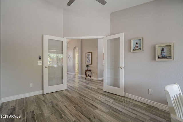 unfurnished room featuring french doors, arched walkways, a ceiling fan, wood finished floors, and high vaulted ceiling