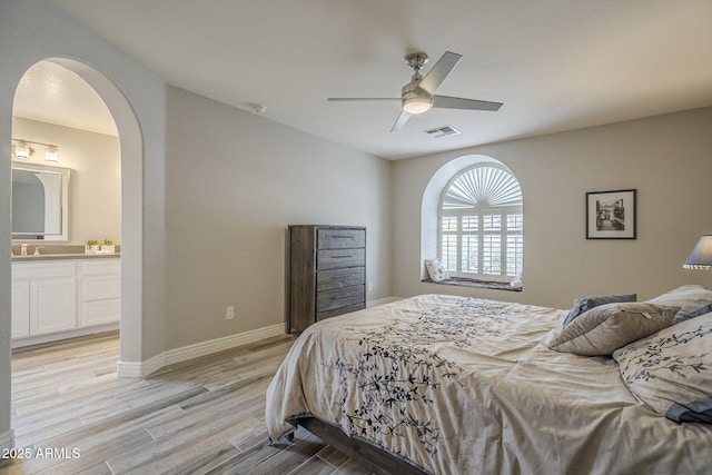 bedroom with arched walkways, light wood finished floors, ensuite bath, baseboards, and a ceiling fan