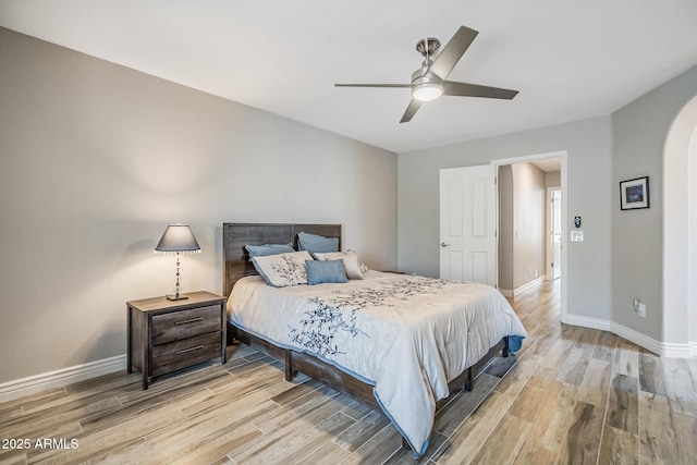 bedroom with arched walkways, light wood-style floors, baseboards, and a ceiling fan