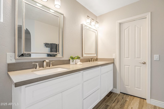 bathroom with wood finished floors, double vanity, and baseboards
