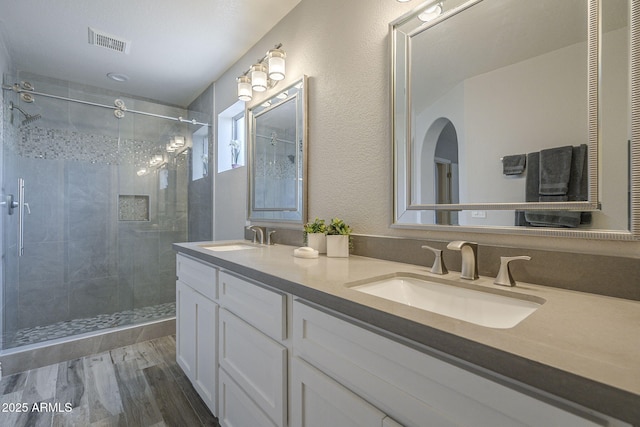 bathroom featuring a shower stall, wood finished floors, and double vanity