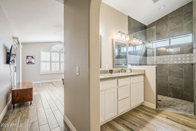 bathroom featuring wood finished floors, lofted ceiling, a walk in shower, vanity, and baseboards